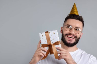 Doğum günün kutlu olsun. Gri arka planda parti şapkası ve hediye kutusu olan yakışıklı bir adam.
