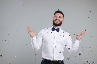 Doğum günün kutlu olsun. Gri arka planda konfeti yağmuru altında parti şapkası takan yakışıklı adam, mesaj için yer var.