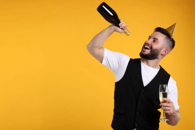 Doğum günün kutlu olsun. Turuncu arka planda parti şapkası ve şampanyası olan yakışıklı bir adam.