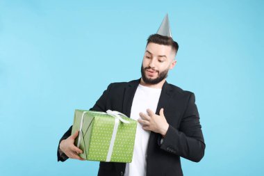 Doğum günün kutlu olsun. Açık mavi arka planda parti şapkası ve hediye kutusu olan yakışıklı bir adam.