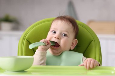 Evdeki beslenme sandalyesinde yemek yiyen şirin bir bebek.