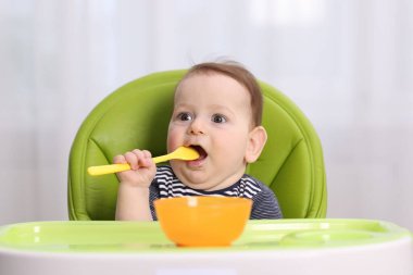Evdeki beslenme sandalyesinde yemek yiyen şirin bir bebek.
