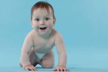 Açık mavi arka planda emekleyen şirin bir bebek.