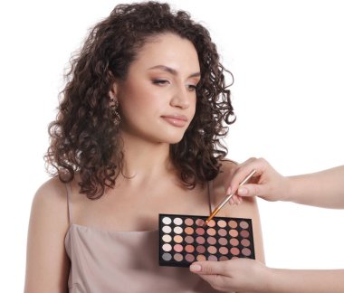 Makyaj sanatçısı beyaz arka planda kadınların yüzüne göz farı uyguluyor.