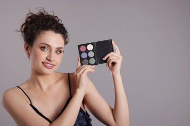 Gri arka planda göz farı paleti olan gülümseyen bir kadın. Metin için boşluk