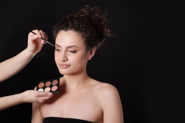 Makyöz, siyah arka planda kadınların yüzüne göz farı takıyor.