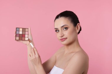 Göz farı paleti ve pembe arka planda fırçası olan kadın