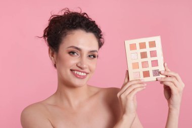 Pembe arka planda göz farı paleti olan gülümseyen kadın.