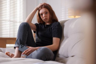 Evdeki kanepede oturan üzgün genç kız.