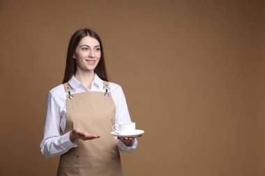 Bej arka planda bir fincan sıcak içecekle gülümseyen barista. Metin için boşluk