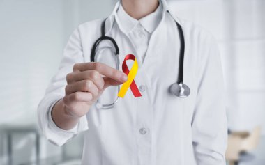 Dünya Hepatit Günü. Bulanık arka planda sarı-kırmızı farkındalık kurdelesi olan doktor, yakın plan.