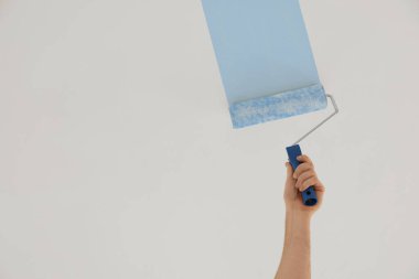 Beyaz adam tavanı açık mavi boyayla boyuyor. Kapalı, düşük açılı.