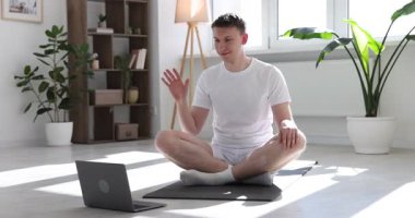 Evdeki laptopla yoga dersinde koçunu selamlayan bir adam.