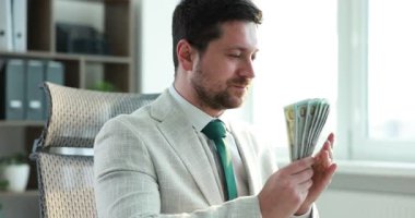 Açgözlü bankacı parayı kokluyor ve ofiste gülümsüyor.