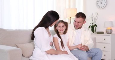 Mutlu ebeveynler ve kızları evdeki kanepede birlikte oturuyorlar.