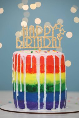 Lezzetli gökkuşağı doğum günü pastası. Üzerinde beyaz masa, açık mavi arka plan, bulanık ışıklar, yakın plan.