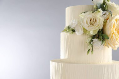 Gri arka planda çiçeklerle süslenmiş lezzetli düğün pastası, yakın plan. Metin için boşluk