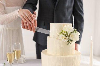 Yeni evliler kapalı bir masada düğün pastasını kesiyorlar.