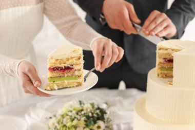 Yeni evliler kapalı bir masada düğün pastası kesiyorlar.