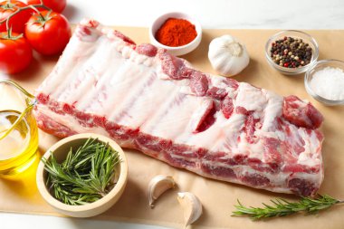 Çiğ domuz kaburgası, baharatlar ve domatesler beyaz masada, yakın plan.