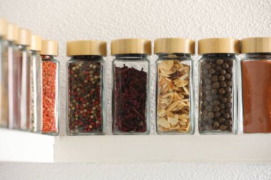 Beyaz raflardaki kavanozlardaki farklı aromatik baharatlar.