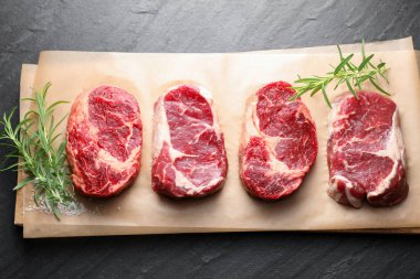 Çiğ et parçaları, biberiye ve tuz siyah masada, üst görünümde.