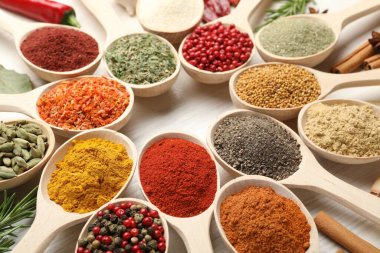 Beyaz ahşap masadaki kaşıklarda farklı aromatik baharatlar, yakın plan.