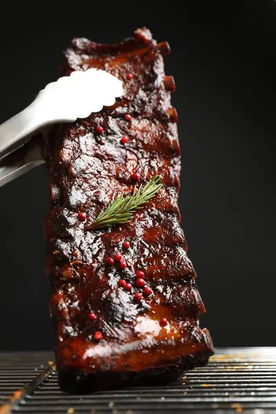 Siyah arka planda ızgaradan maşayla leziz domuz pirzolası alıp yakın plan çekiyoruz.