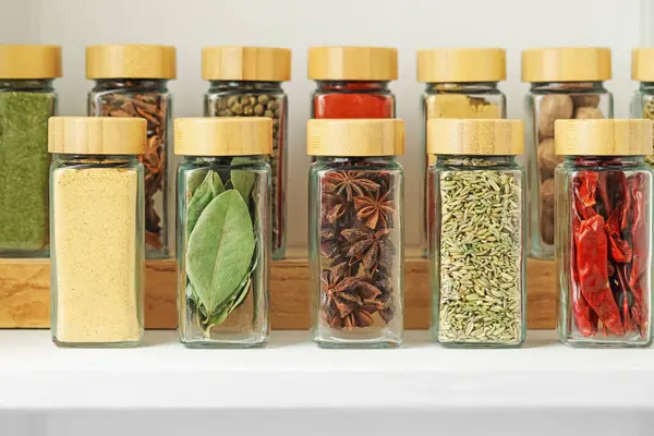 Beyaz masadaki kavanozlardaki farklı aromatik baharatlar, yakın plan.