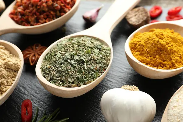Siyah masada kaşıklardaki farklı aromatik baharatlar, yakın plan.