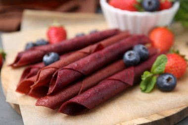 Lezzetli meyve dürümleri, çilekler, yaban mersinleri ve nane şekeri gri ahşap masada, yakın plan.