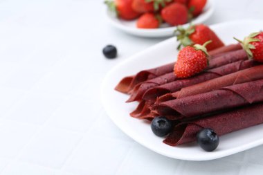 Lezzetli meyve dürümleri, çilekler ve yaban mersinleri beyaz masada, yakın plan. Metin için boşluk