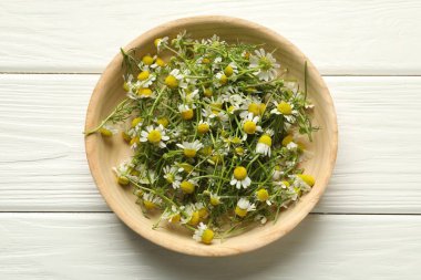 Beyaz ahşap masada kasede taze papatya çiçekleri.