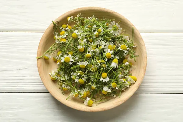 Beyaz ahşap masada kasede taze papatya çiçekleri.