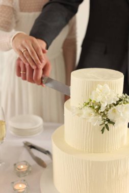 Yeni evliler kapalı bir masada düğün pastasını kesiyorlar.