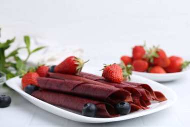 Lezzetli meyve dürümleri, çilekler ve yaban mersinleri beyaz masada, yakın plan. Metin için boşluk