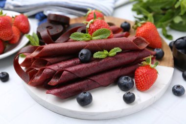 Lezzetli meyve dürümleri, çilekler, yaban mersini ve nane şekeri beyaz masada, yakın plan.