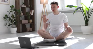 Evdeki laptopla yoga dersinde koçunu selamlayan bir adam.
