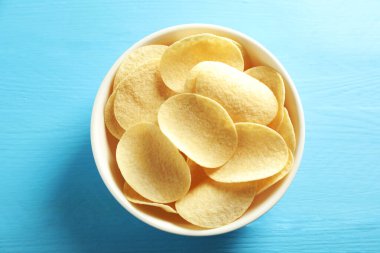 Açık mavi ahşap masada, tabakta patates cipsi.