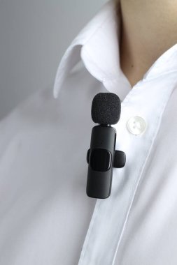 Gri arka planda gömleğine mikrofon takmış bir adam.