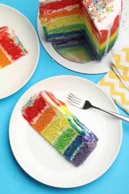 Açık mavi masada servis edilen leziz gökkuşağı pastasından parçalar.