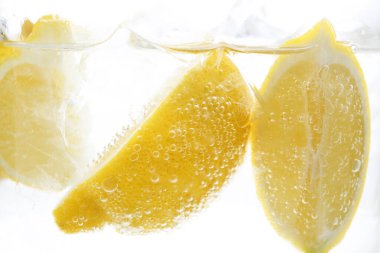 Beyaz arka planda limon dilimleri ile soda tazeleniyor, yakın plan.