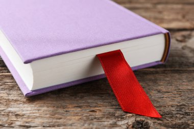 Ahşap masada kırmızı kurdele yer imi olan bir kitap, yakın plan.