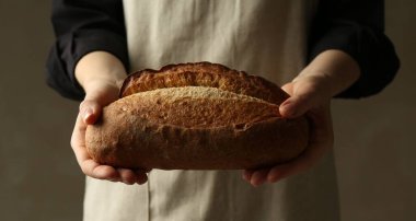 Gri arka planda taze ekmek somunu olan kadın, yakın plan.