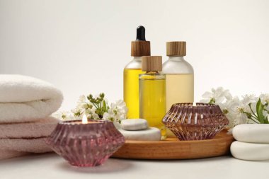 Spa ürünleri, yanan mumlar, çakıl taşları ve beyaz masadaki güzel çiçekli dallar, yakın plan.