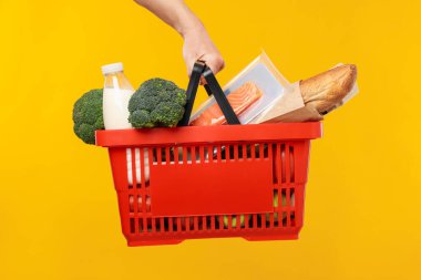 Sarı arka planda farklı ürünleri olan alışveriş sepeti tutan adam, yakın plan.