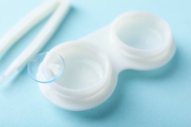 Açık mavi arkaplanda kontak lensler, bavul ve cımbızlar, yakın plan