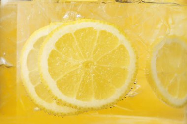 Sarı arka planda limon dilimleri ve buzla soda tazeleniyor. Yakın plan.
