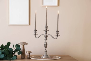 Havalı şamdanlar, yanan mumlar ve bej duvarın yanındaki ahşap masa üzerindeki diğer dekorlar.