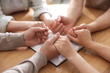 İncilli aile ahşap masada dua ediyor, yakın plan.